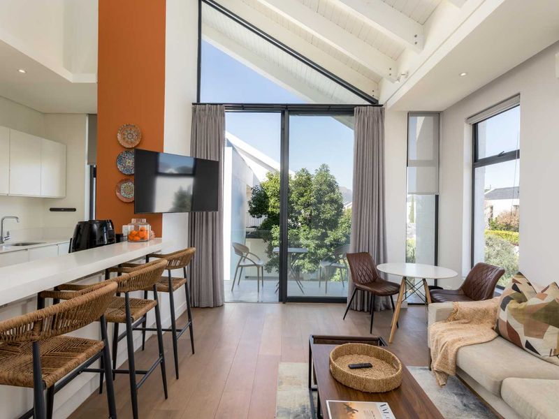 Modern open-plan living area featuring a sleek kitchen with stone countertops, vaulted ceilings with exposed rafters, and large sliding doors leading to a balcony.
