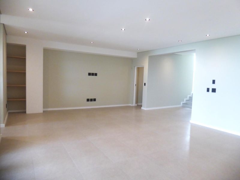 A spacious, empty living area featuring neutral tiled flooring, recessed downlights, and built-in shelving, offering a clean and versatile space for interior design.