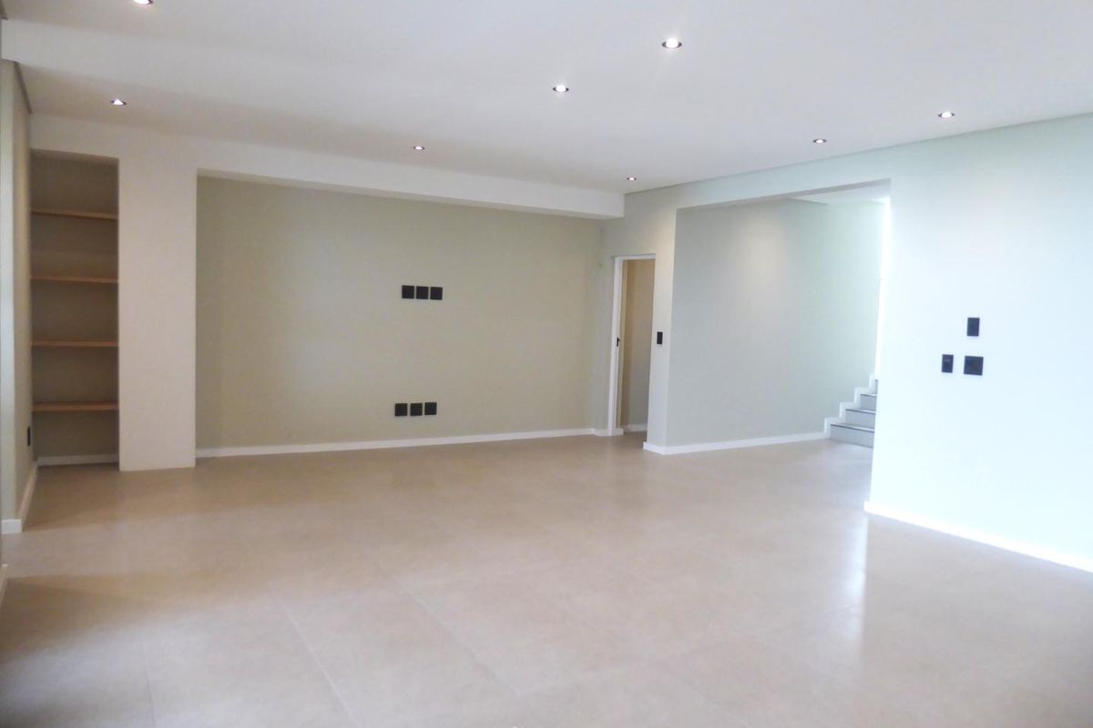 A spacious, empty living area featuring neutral tiled flooring, recessed downlights, and built-in shelving, offering a clean and versatile space for interior design.