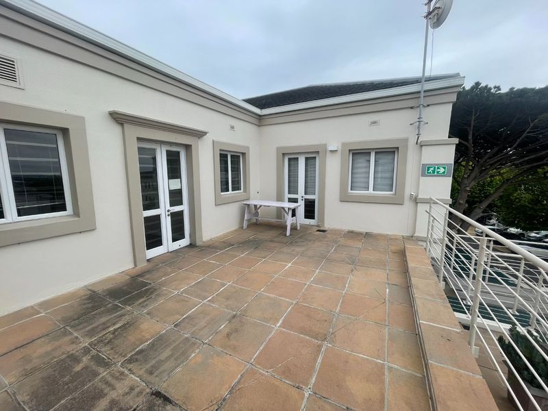 A spacious outdoor balcony area featuring tiled flooring, metal safety railings, and direct access to the office interior through double glass doors.
