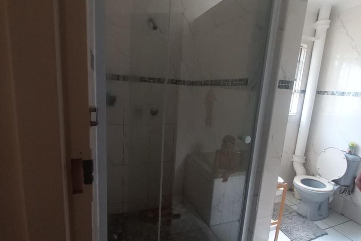 A functional bathroom featuring a glass-enclosed shower, a bathtub, and a standard toilet with white tiled walls and flooring.