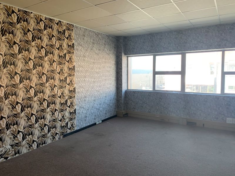 An empty office space featuring large windows, patterned wallpaper, and a suspended ceiling, offering a blank canvas for professional workspace customization.