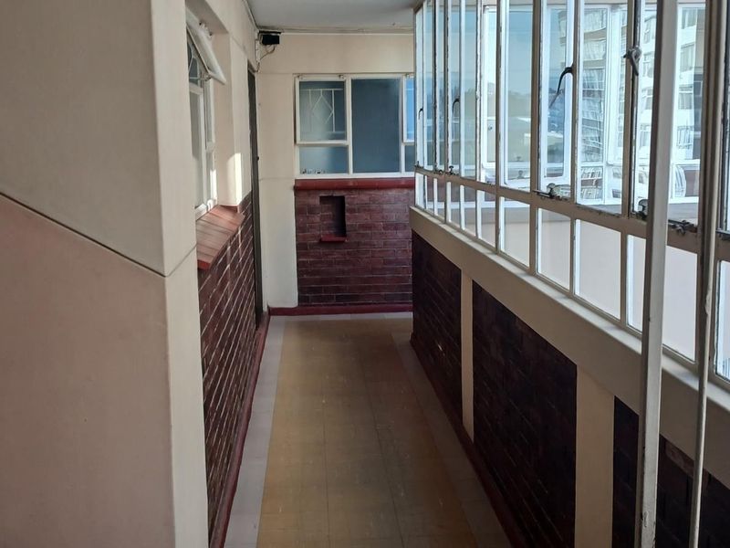 An enclosed balcony area featuring brick wall accents, tiled flooring, and large windows, offering a functional transition space with potential for modernization.