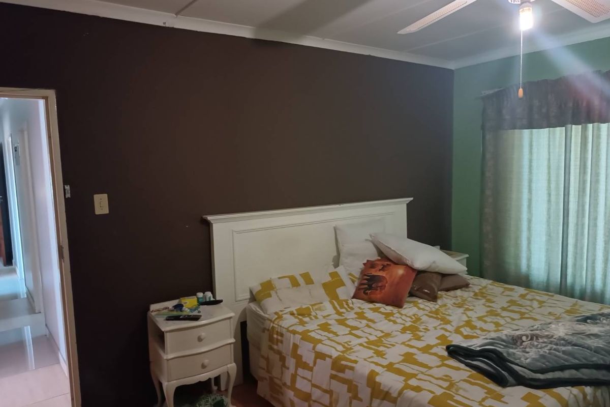 A bedroom featuring a ceiling fan and coving, with a dark accent wall and a view into the adjacent hallway.