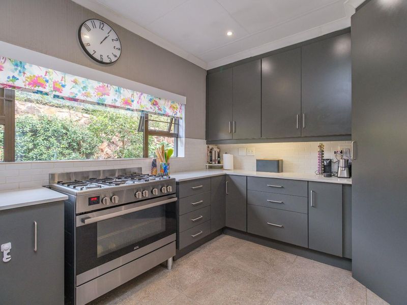 Modern kitchen featuring dark grey cabinetry, stone countertops, a gas stove with oven, and a subway tile backsplash with a garden view.