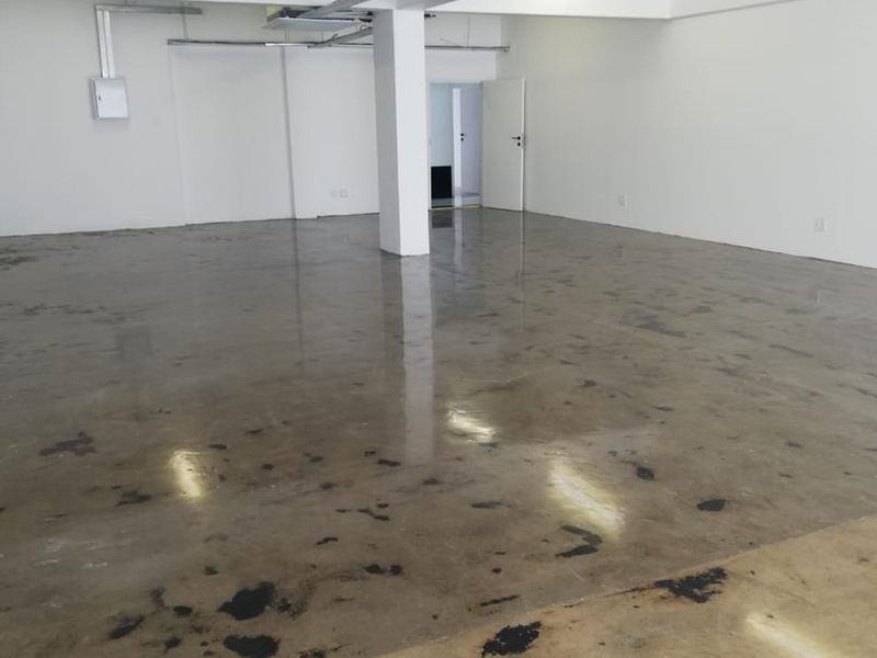 An open-plan office space featuring polished concrete floors, exposed ceiling lighting, and a central support column, providing a versatile blank canvas for business operations.