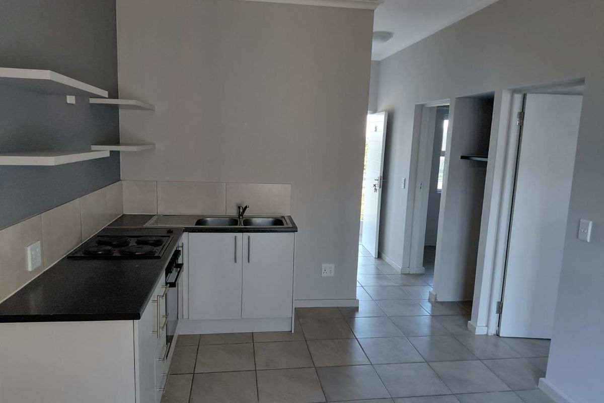 A clean, functional kitchen featuring white cabinetry, dark countertops, a built-in hob and oven, and neutral tiled flooring in an open-plan layout.