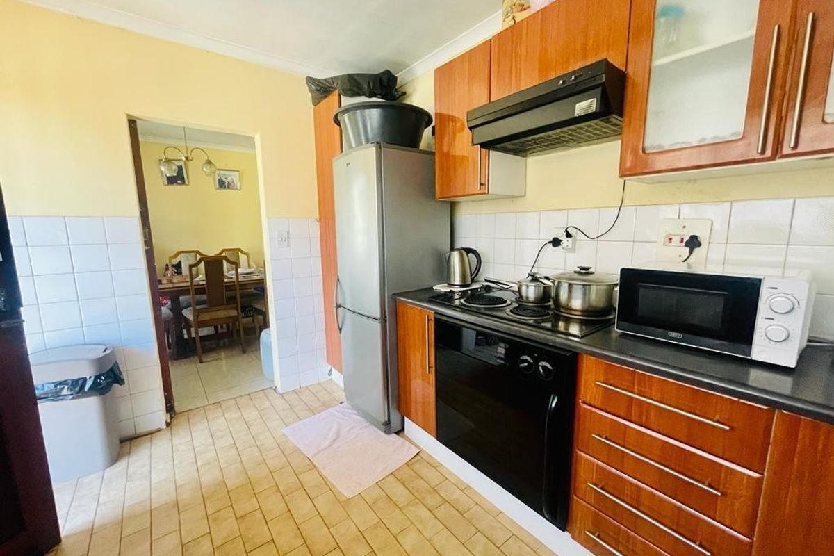 A functional kitchen featuring wood-finish cabinetry, built-in oven and hob, tiled splashbacks, and direct access to the adjacent dining area.