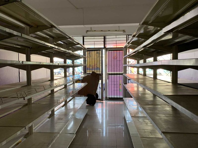 A vacant retail utility space featuring extensive metal shelving units, tiled flooring, and a glass entrance door with security gate.