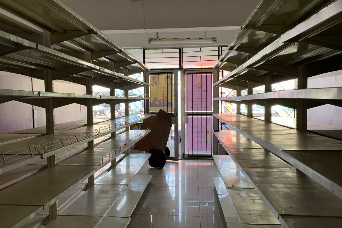 A vacant retail utility space featuring extensive metal shelving units, tiled flooring, and a glass entrance door with security gate.