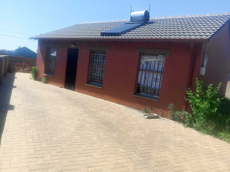 Front exterior view of a single-story house featuring a paved driveway, tiled roof, and installed solar water heating system.