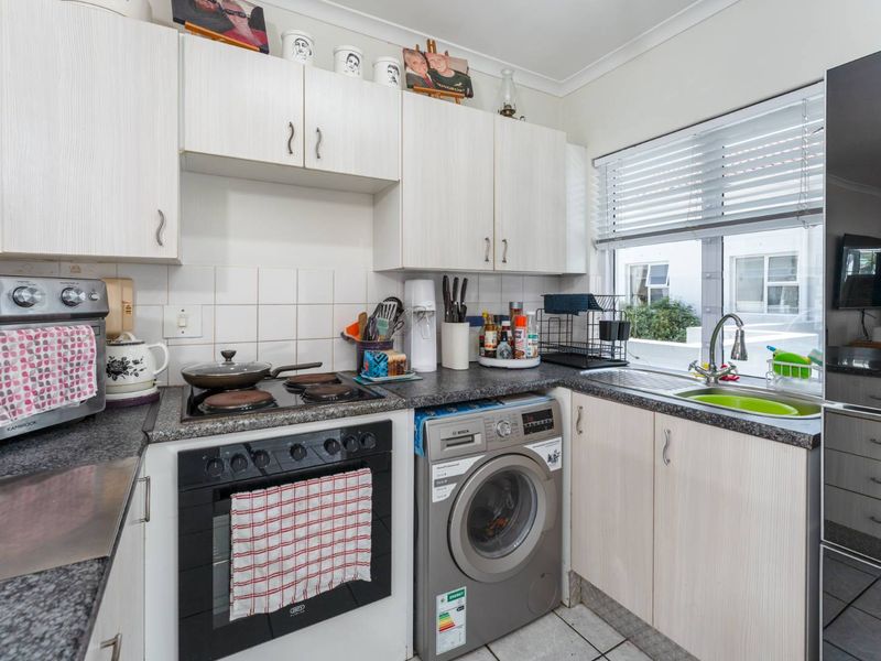Compact kitchen featuring light-toned cabinetry, granite-look laminate countertops, integrated electric oven and hob, and a stainless steel sink with a window view.