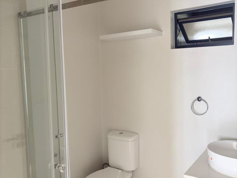 A clean, modern bathroom featuring a glass shower enclosure, a vanity with a vessel sink, and neutral tiled flooring.