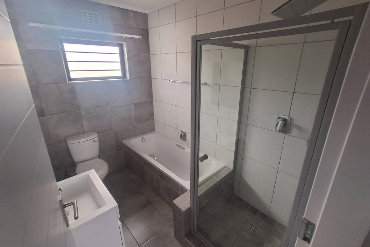 Modern bathroom featuring a built-in bathtub, separate glass-enclosed shower with rain shower head, wall-mounted vanity, and neutral grey and white tiled finishes.