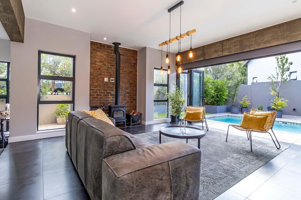Modern living room featuring a brick fireplace, large windows, and seamless indoor-outdoor flow to a private patio and swimming pool area.