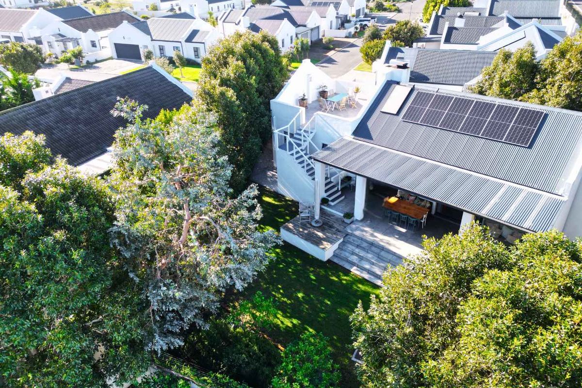 Aerial view of a residential property featuring a corrugated metal roof with solar panels, a roof terrace with a spiral staircase, and a covered patio.