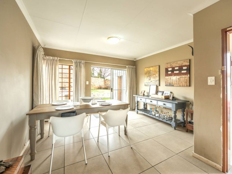 A bright dining room featuring neutral tiled flooring, coved ceilings, and a sliding glass door providing direct access to the rear garden area.