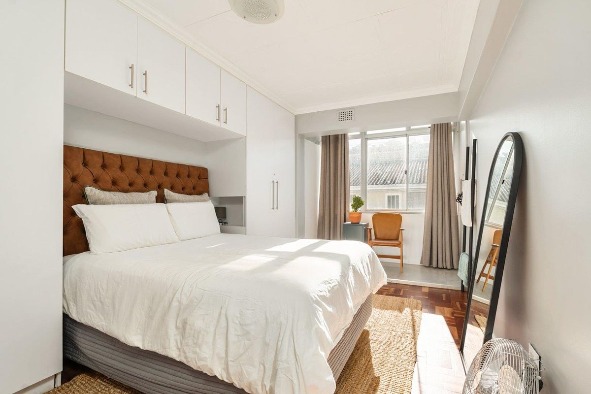 A well-lit bedroom featuring parquet flooring, extensive built-in cabinetry with overhead storage, and large windows allowing for natural light.