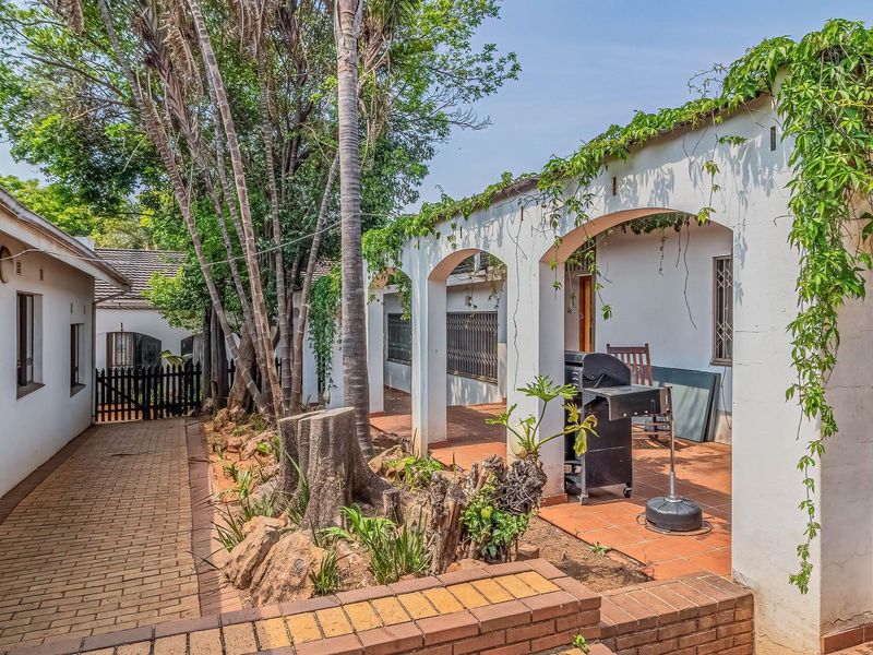 A covered outdoor patio area featuring arched architectural details, terracotta tiling, and direct access to a paved garden walkway.