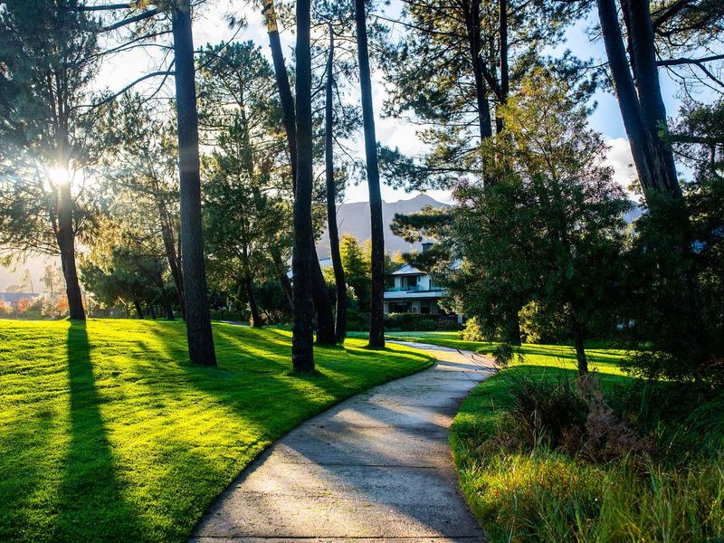 A beautifully landscaped garden area featuring a winding paved pathway surrounded by mature trees and well-maintained green lawns.