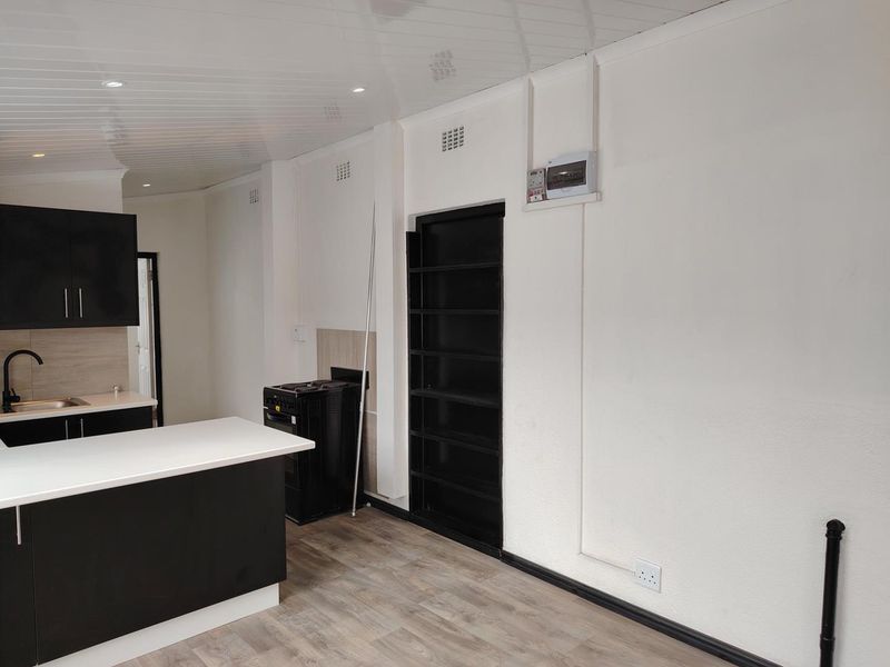 Open plan kitchen area featuring modern black cabinetry, a central island, and laminate flooring in a clean, minimalist space.