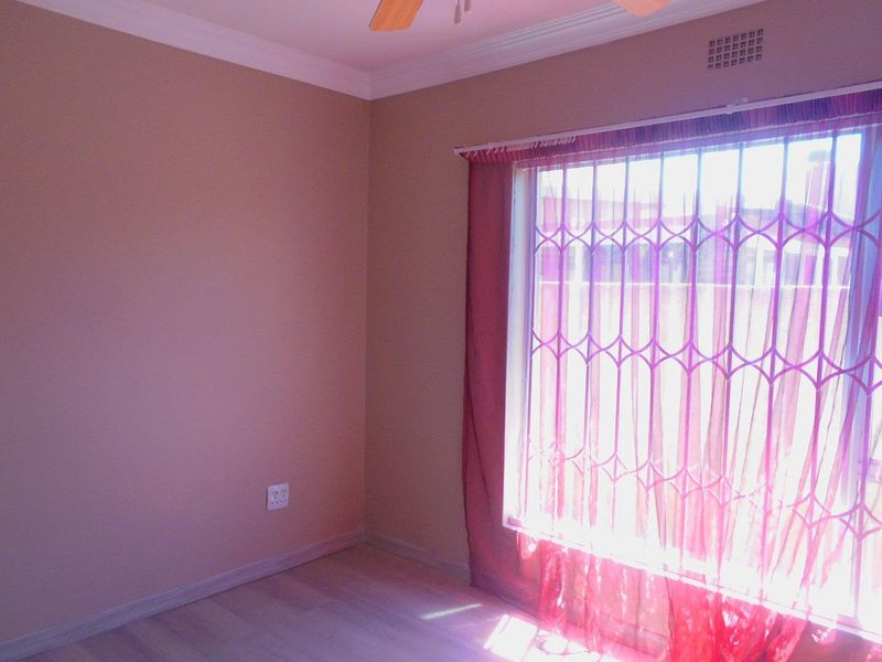 A bright, empty bedroom featuring laminate flooring, a ceiling fan, and a window fitted with a security gate.