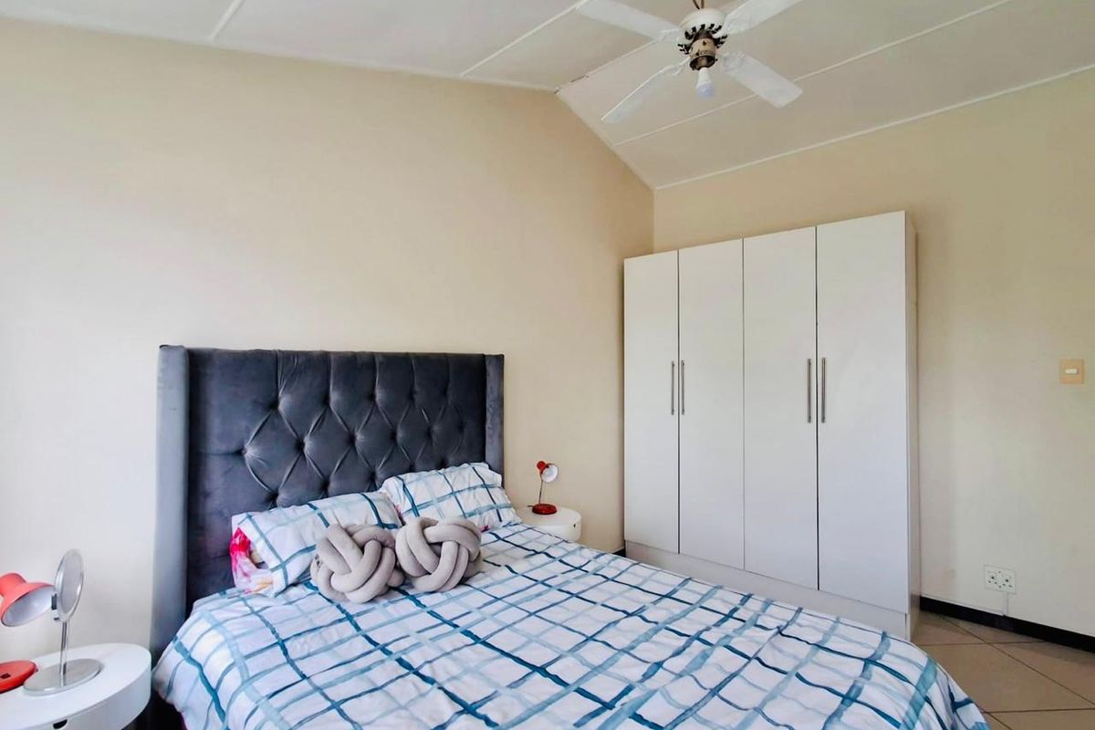 A bedroom featuring a built-in wardrobe, ceiling fan, and tiled flooring, offering a functional and neutral living space.