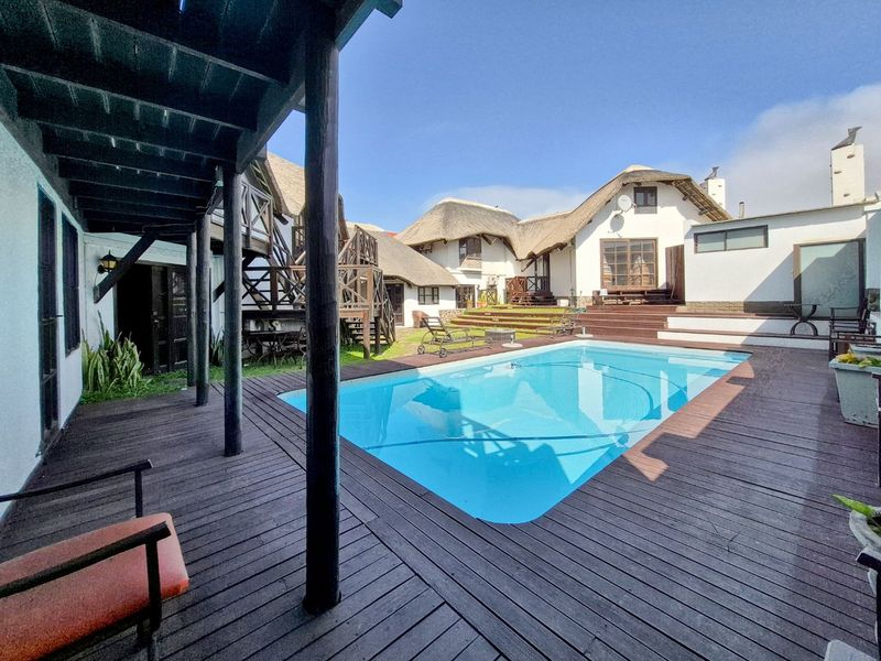 Outdoor pool area featuring extensive timber decking, thatched roof structures, and multi-level access stairs in a courtyard setting.