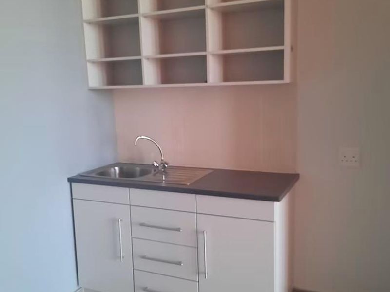 A clean and functional scullery area featuring white built-in cabinetry, open shelving, a stainless steel sink, and a dark laminate countertop.