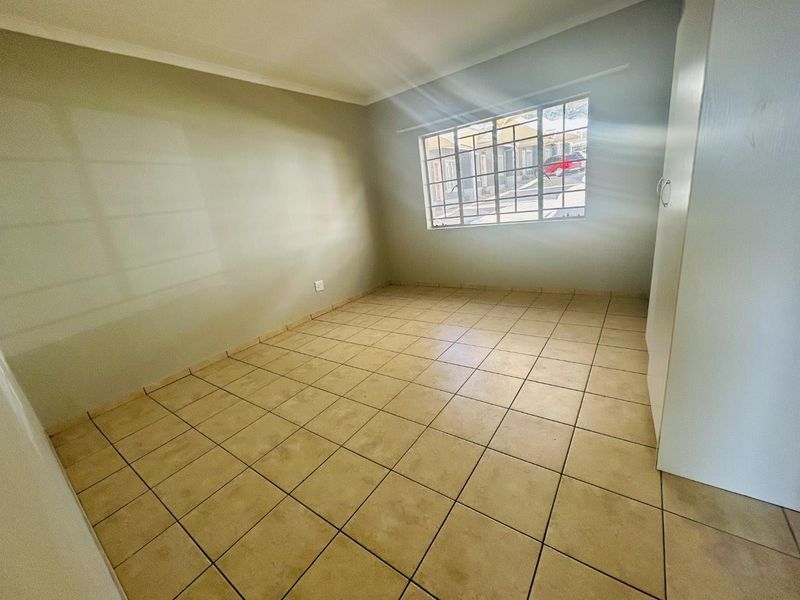 A vacant bedroom featuring neutral wall tones, tiled flooring, and a built-in cupboard, offering a clean canvas for personalization.