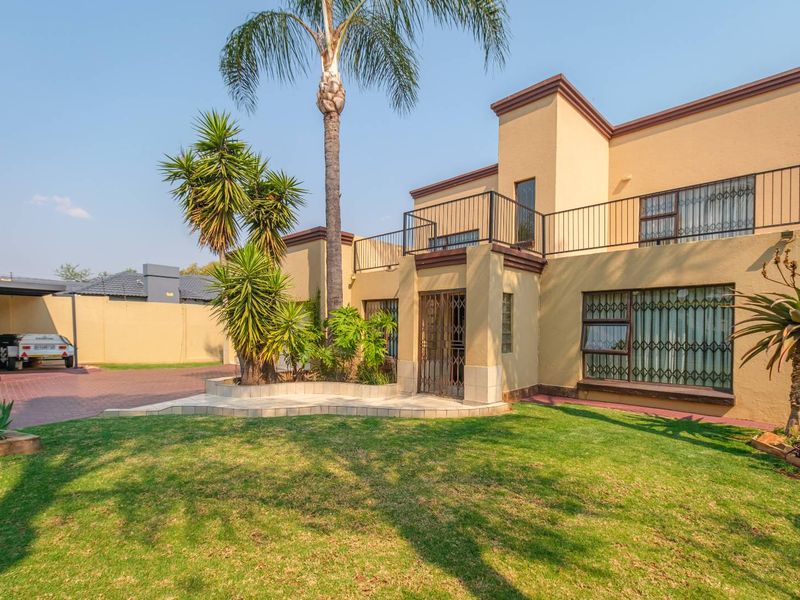 Front view of a two-story residential property featuring a paved driveway, carport, landscaped garden, and an upper-level balcony with security features.