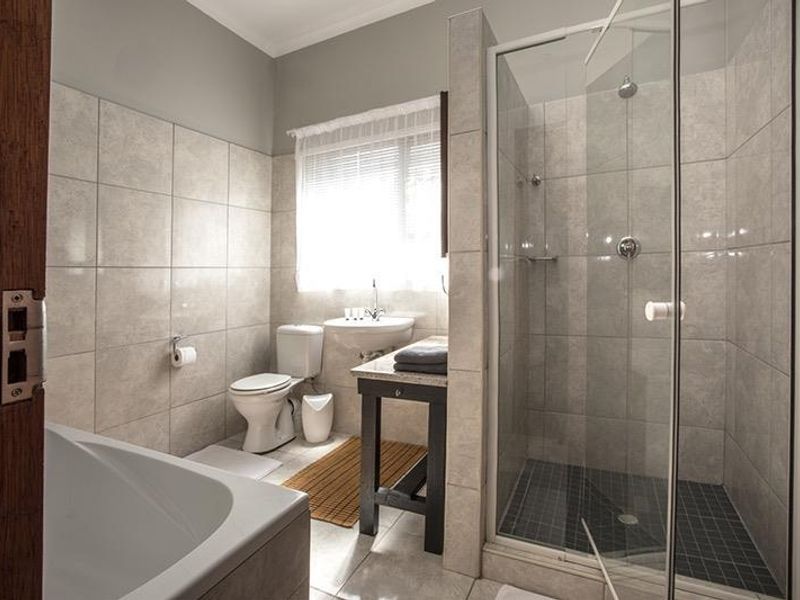 A well-maintained bathroom featuring a glass-enclosed shower, a bathtub, a toilet, and a vanity basin with neutral wall and floor tiling.