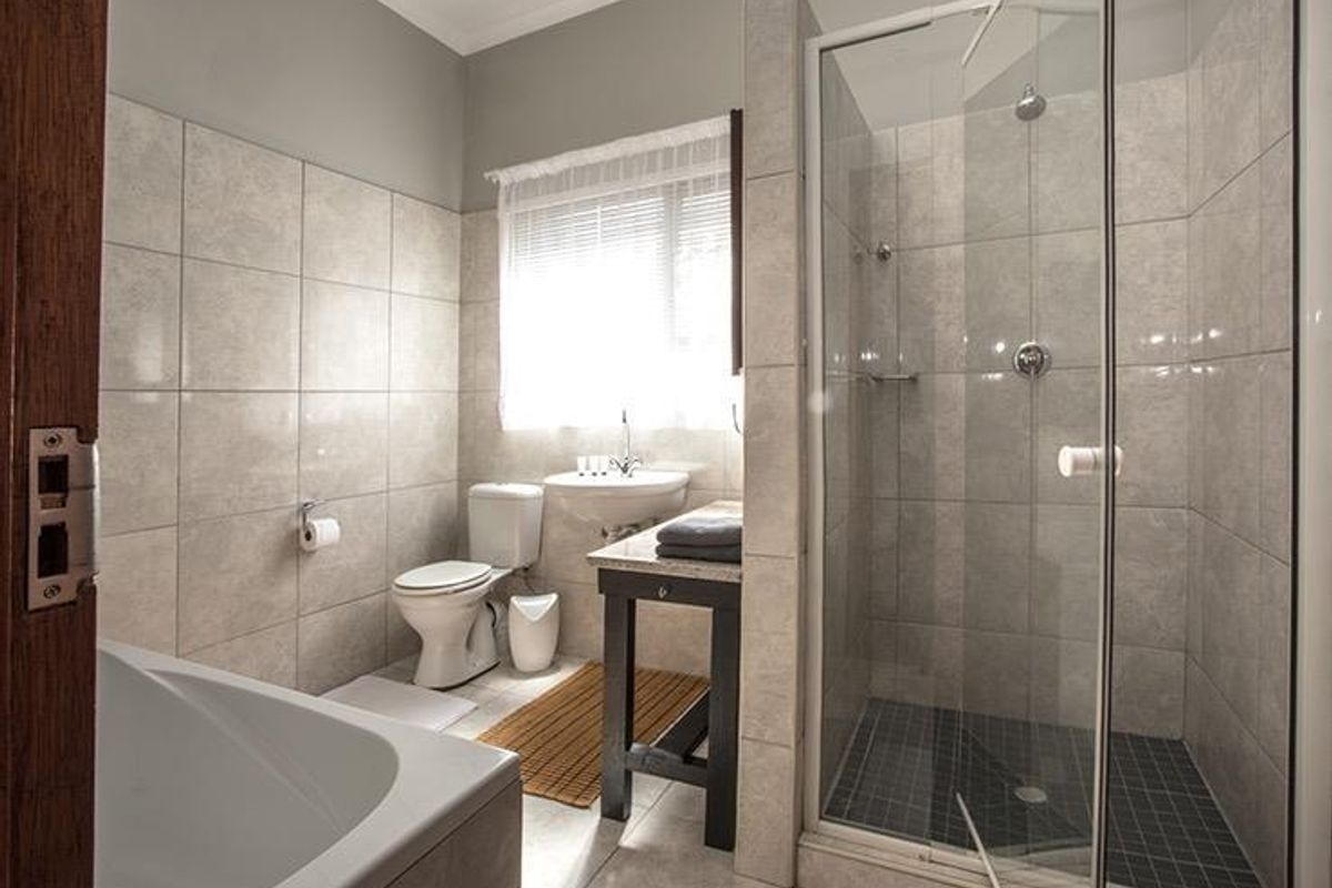 A well-maintained bathroom featuring a glass-enclosed shower, a bathtub, a toilet, and a vanity basin with neutral wall and floor tiling.