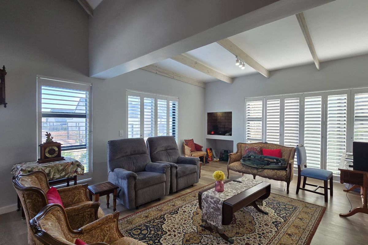 Spacious living room featuring a vaulted ceiling with exposed timber beams, plantation shutters, and a built-in fireplace alcove.