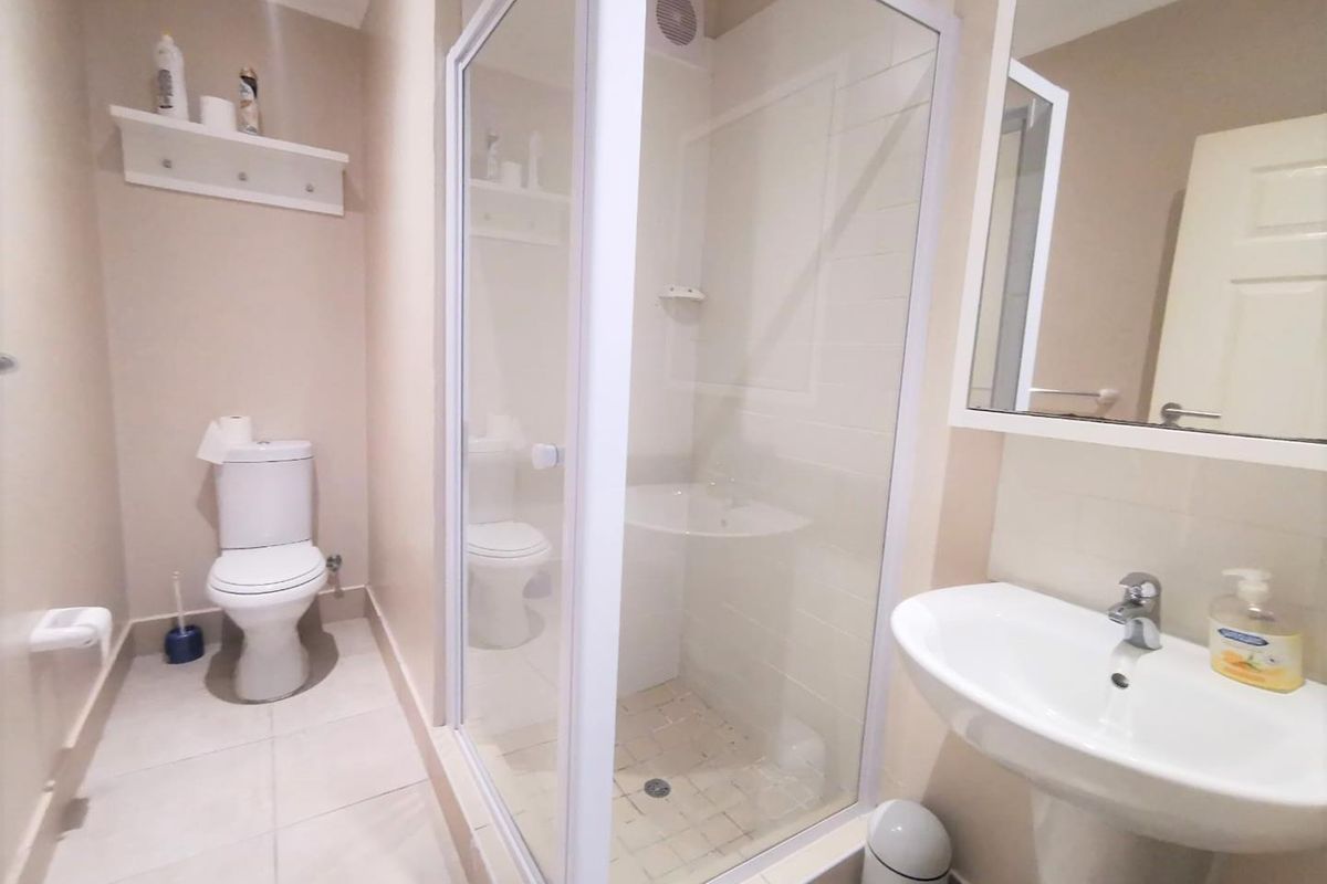 A clean and functional bathroom featuring a glass shower enclosure, pedestal basin, toilet, and wall-mounted mirror with neutral tiled flooring.