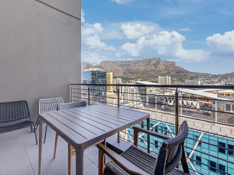 A modern balcony featuring tiled flooring and a stainless steel balustrade, offering expansive urban views with Table Mountain in the background.
