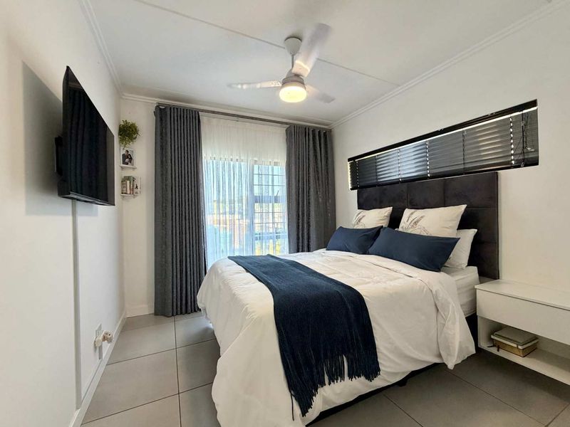 A well-maintained bedroom featuring tiled flooring, a ceiling fan, and a sliding glass door with integrated curtain tracks and horizontal blinds.
