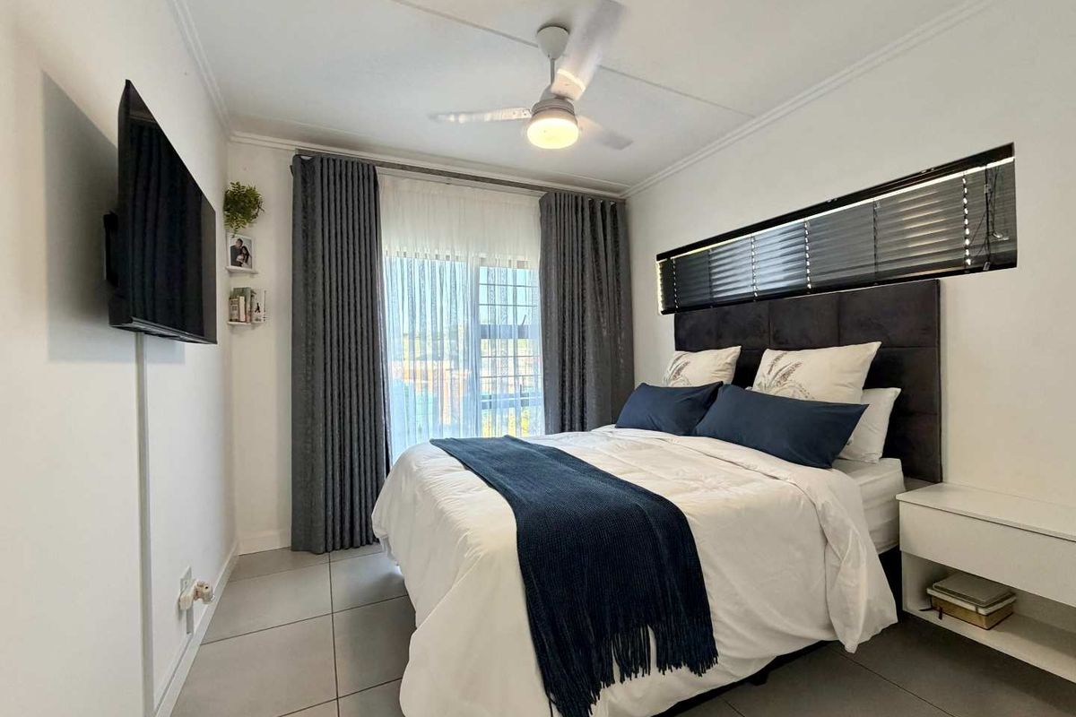 A well-maintained bedroom featuring tiled flooring, a ceiling fan, and a sliding glass door with integrated curtain tracks and horizontal blinds.