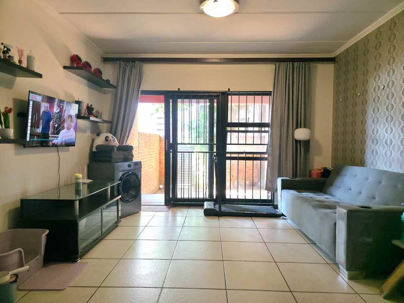 A living room featuring tiled flooring, a feature wallpaper wall, and a sliding door with a security gate leading to an outdoor area.