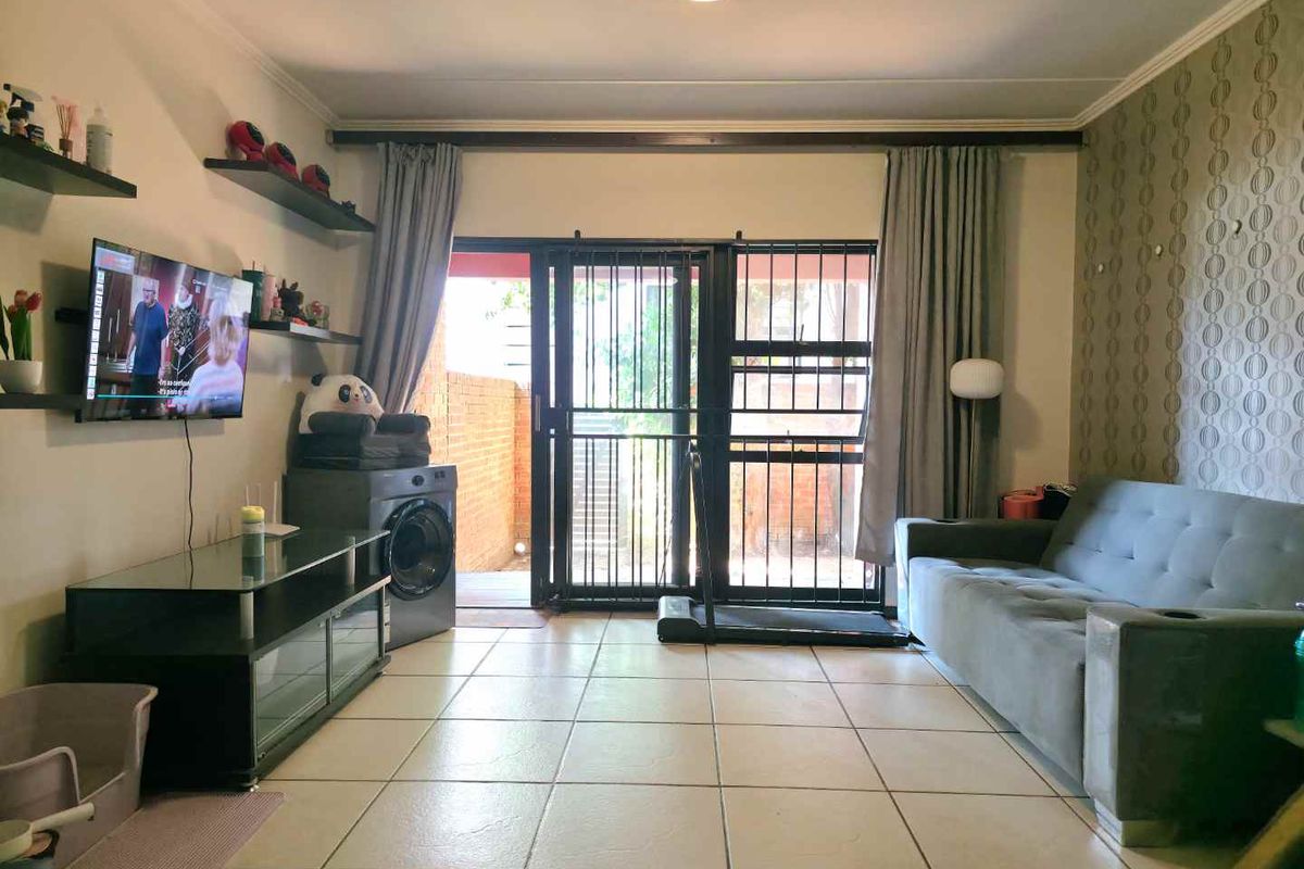 A living room featuring tiled flooring, a feature wallpaper wall, and a sliding door with a security gate leading to an outdoor area.