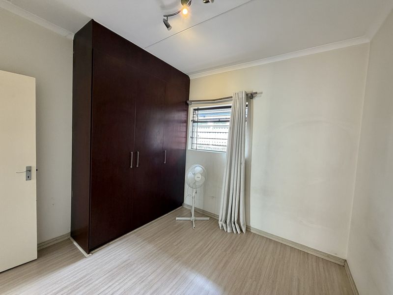 A bedroom featuring laminate flooring, a large dark wood built-in wardrobe, and security bars on the window.