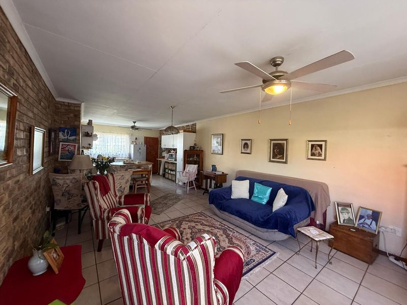 Spacious open-plan living and dining area featuring tiled flooring, an exposed brick feature wall, and a ceiling fan, flowing into the kitchen space.