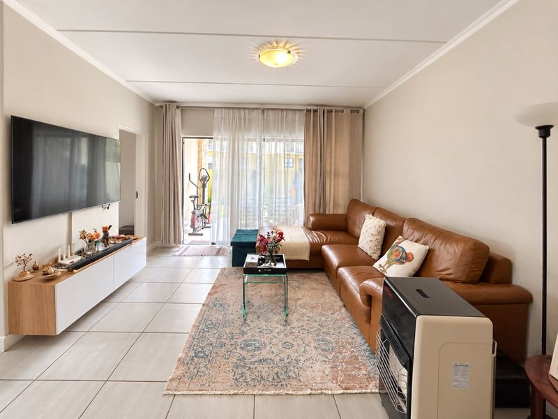 A bright and spacious living room featuring neutral tiled flooring, coving, and a large sliding glass door providing access to an outdoor patio area.