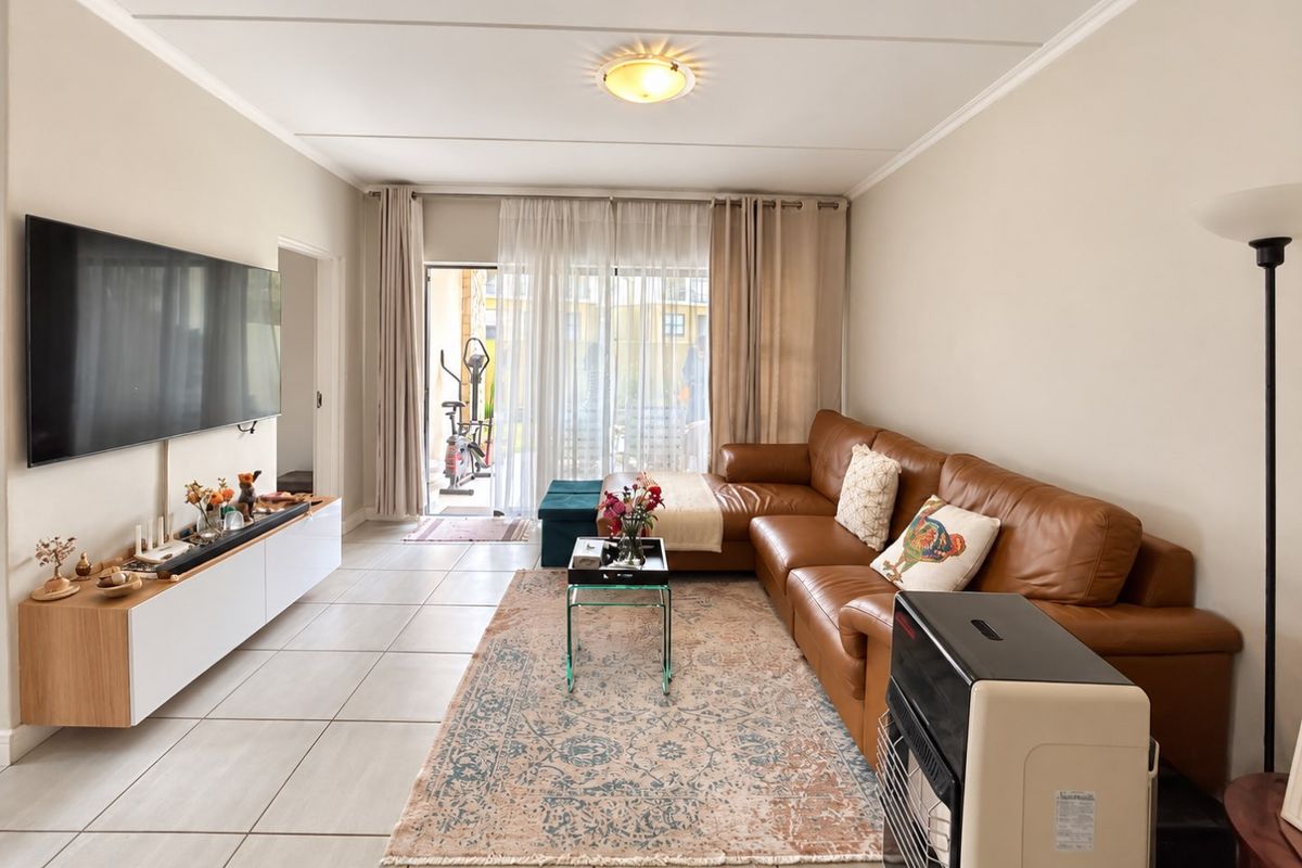 A bright and spacious living room featuring neutral tiled flooring, coving, and a large sliding glass door providing access to an outdoor patio area.