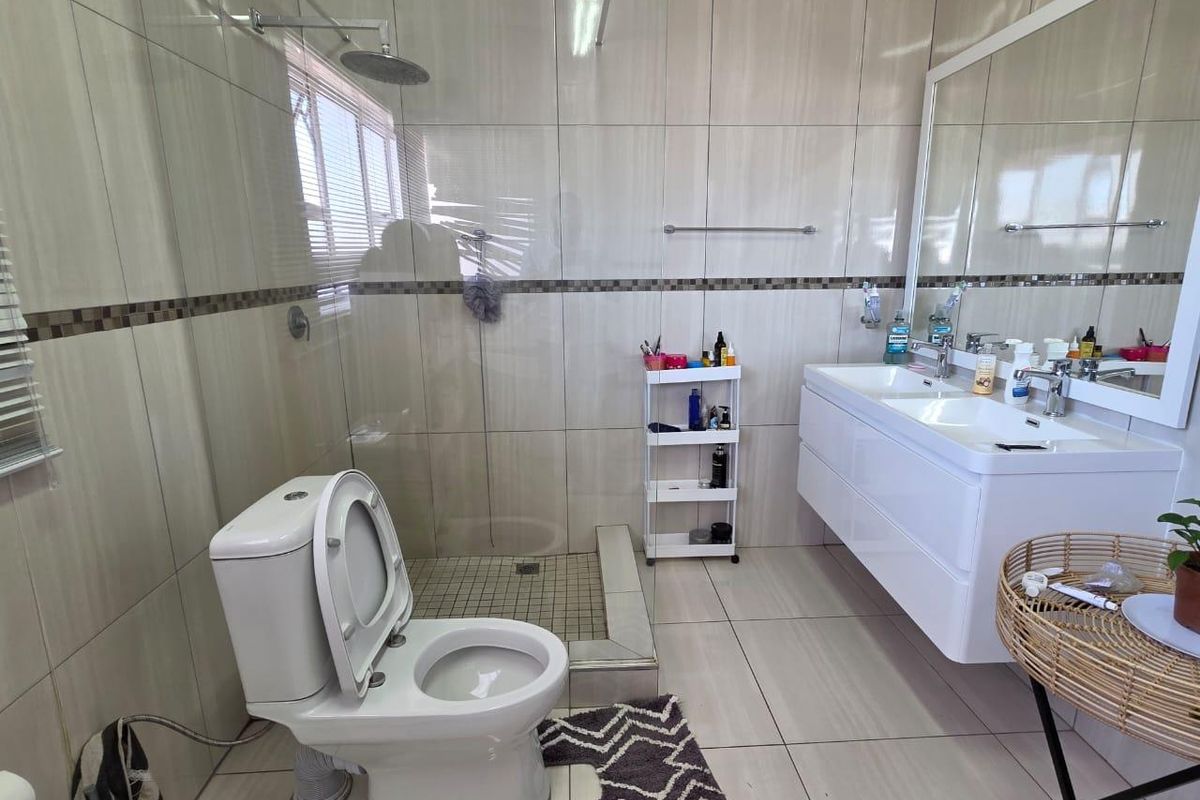 Modern bathroom featuring a double vanity, walk-in shower with glass partition, and floor-to-ceiling tiling.