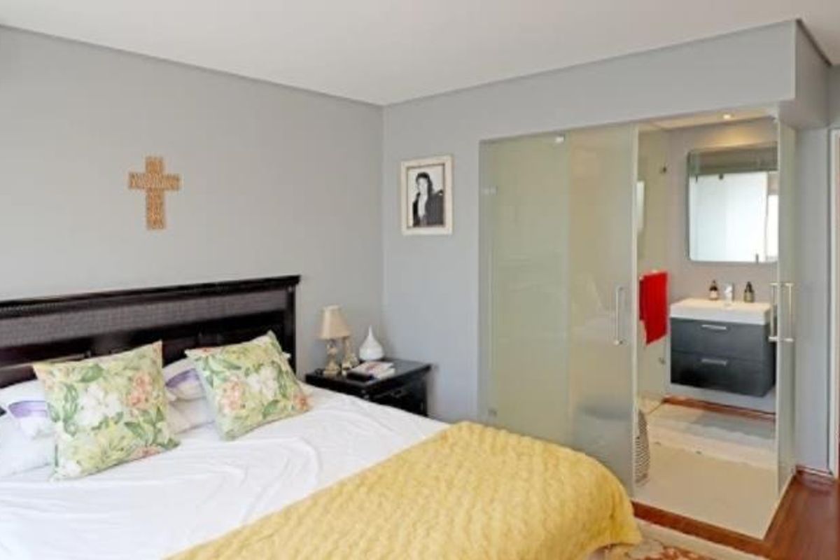 Spacious bedroom featuring an integrated en-suite bathroom with a modern wall-mounted vanity and frosted glass partition, complemented by hardwood flooring and neutral wall tones.