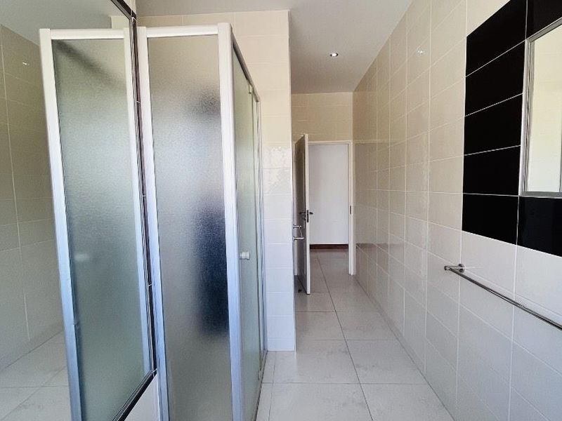 A clean, modern bathroom featuring a glass shower enclosure, neutral wall and floor tiling, and recessed lighting.