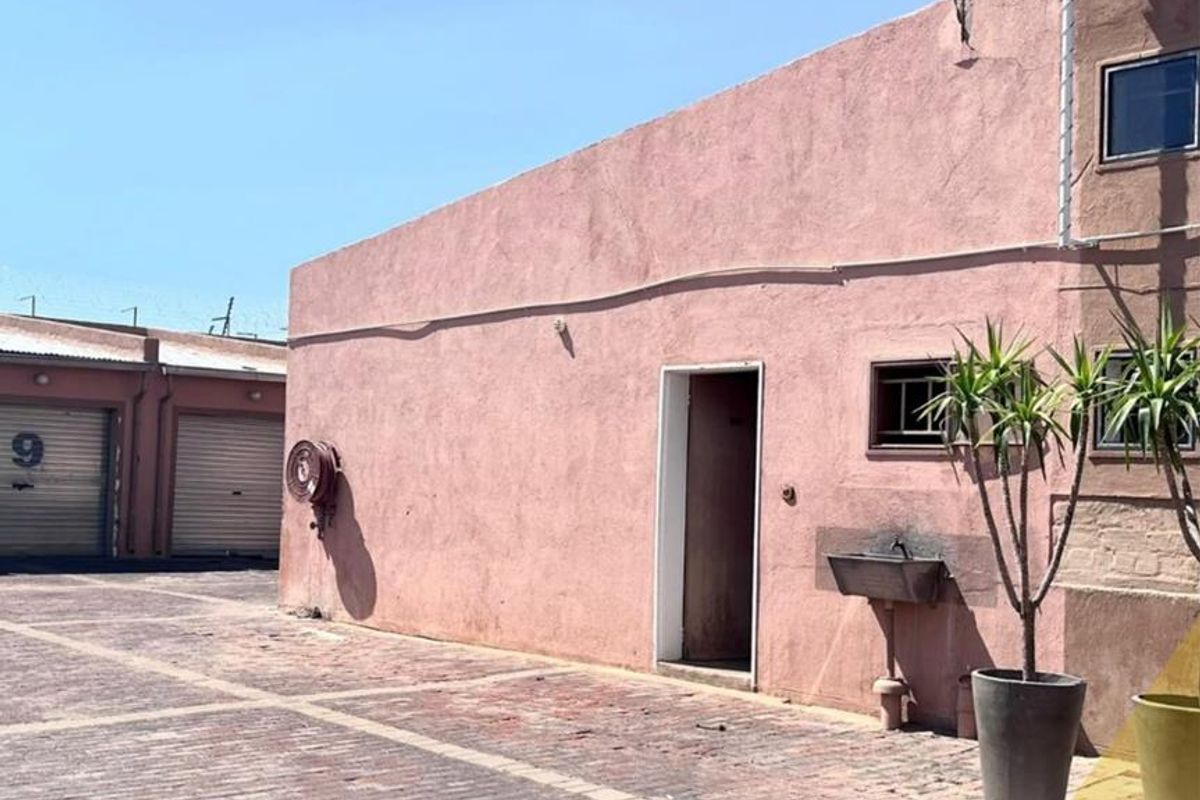 Exterior view of a mixed-use property featuring a paved courtyard, wall-mounted fire hose reel, and a utility sink.