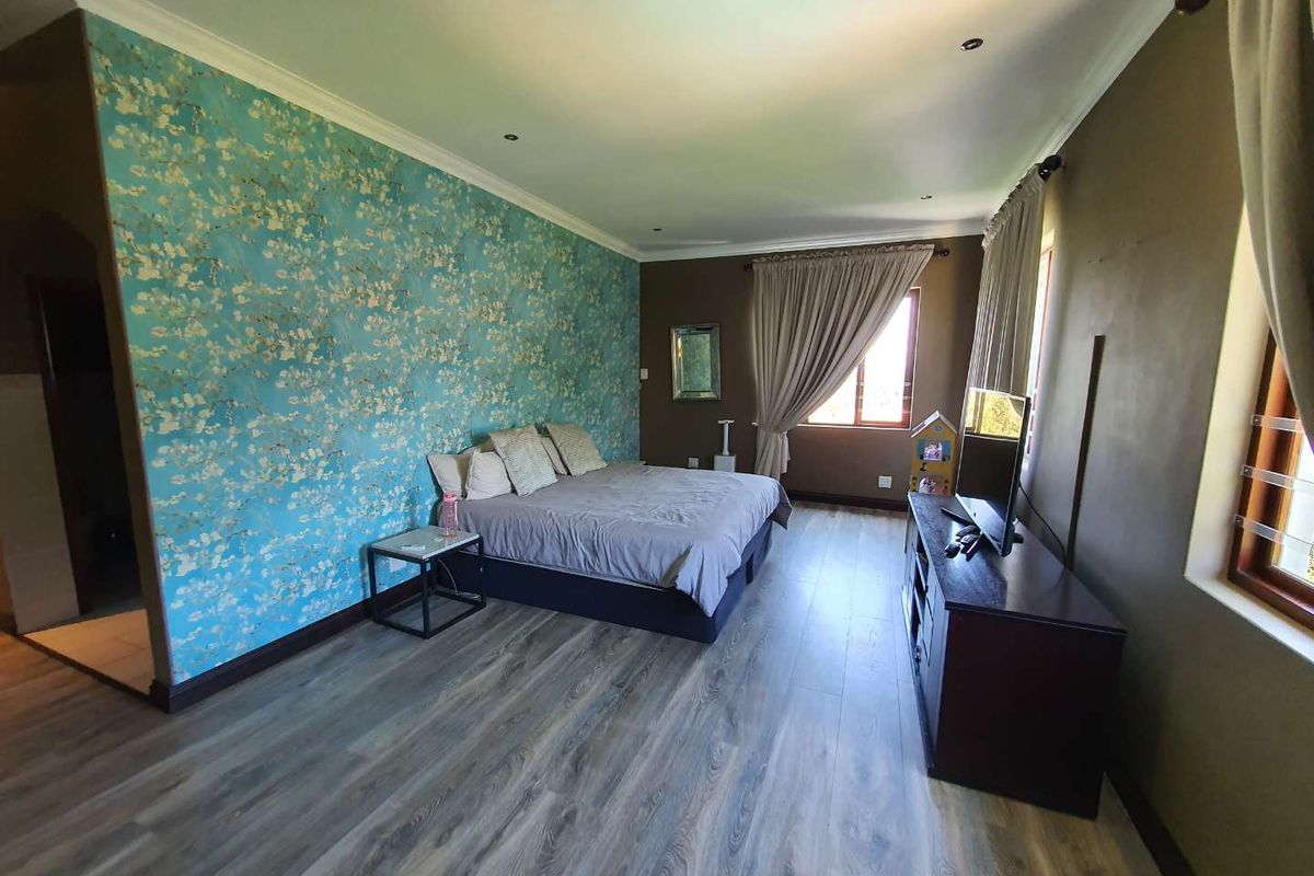 Spacious bedroom featuring modern laminate flooring, recessed downlighting, and a decorative feature wall with floral wallpaper.