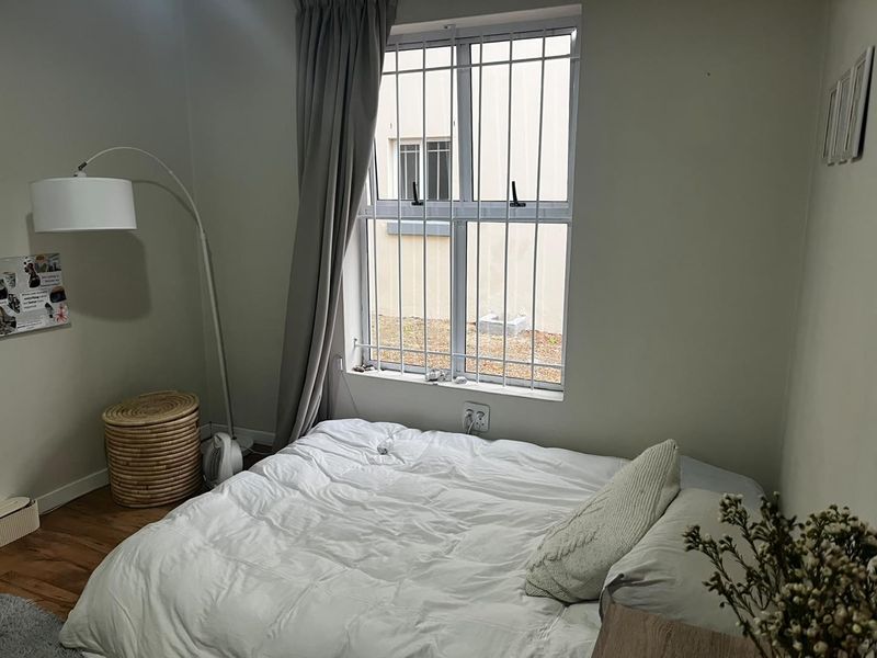 A cozy bedroom featuring laminate flooring and a window fitted with security bars, providing natural light and a view of the exterior.